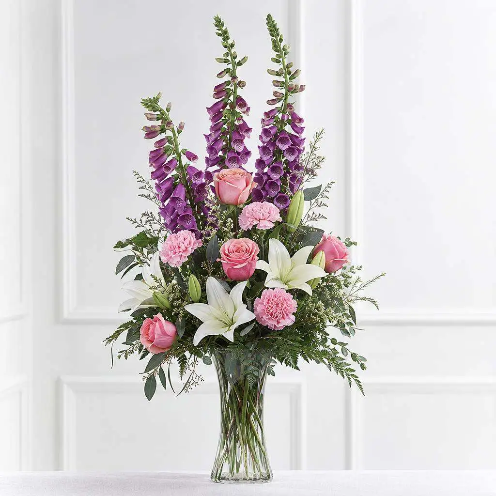 Tall clear vase sympathy spray with purple foxglove spires, pink roses, and pink carnations