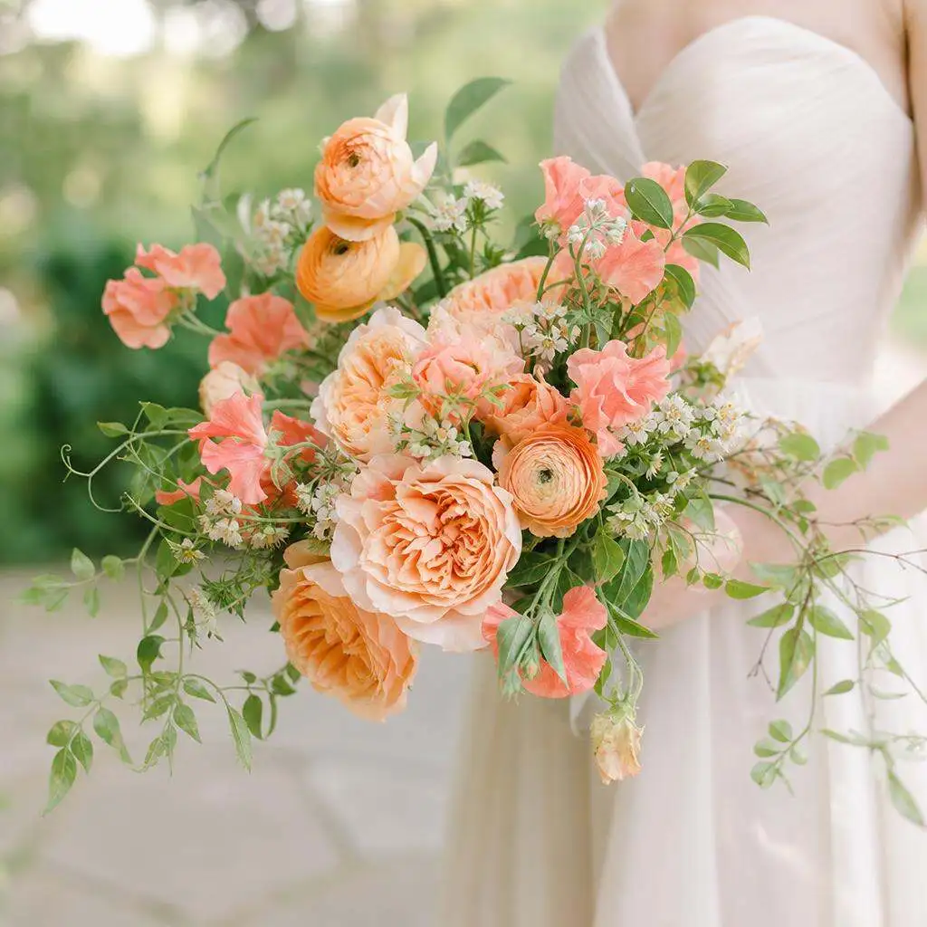 Garden-gathered bridal bouquet in peach, apricot, and coral held by a bride in an ivory gown